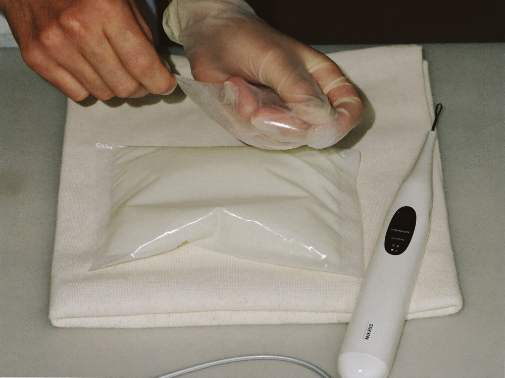 Gloved hands opening sealed single-use sachet beside handpiece