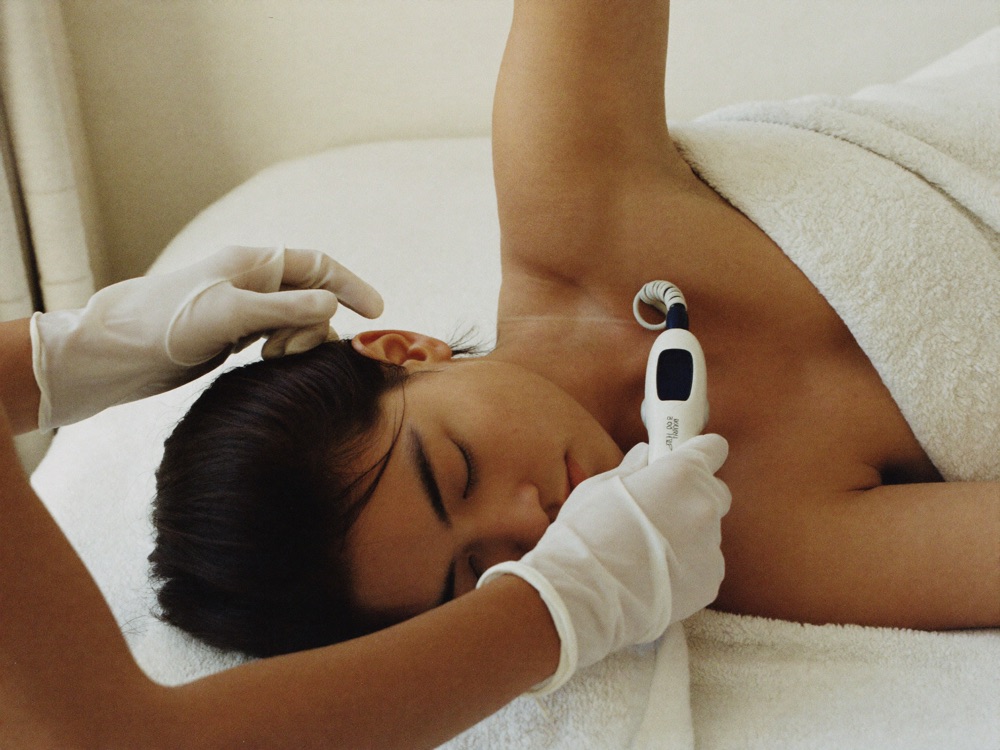 Therapist performing underarm laser pass on draped guest